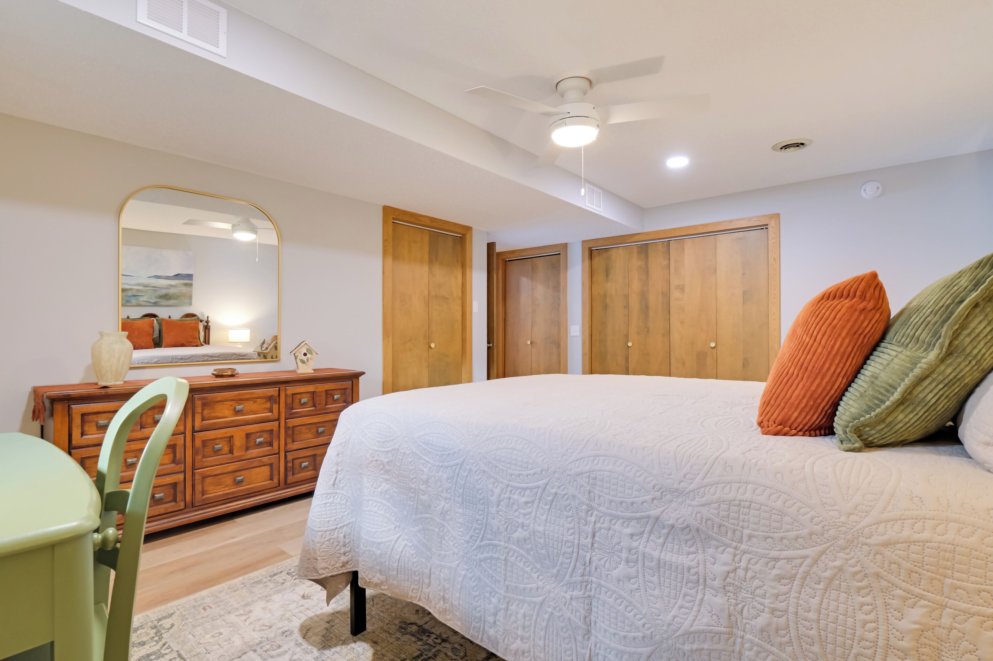 Een slaapkamer met een groot bed, een houten garderobe, een dressoir en een spiegel.