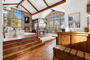 A spacious living area with a fireplace, wooden staircase, and large windows offering views of the outdoors. - Whispering Pines🌲Luxury Keystone Retreat 🏔️ Hot Tub 🛁 Game Room ⛷️ 1 Mile to Lifts (Keystone)