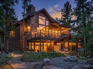 Eine zweistöckige Holzhütte mit Balkon, großen Fenstern und einem Steinofen.