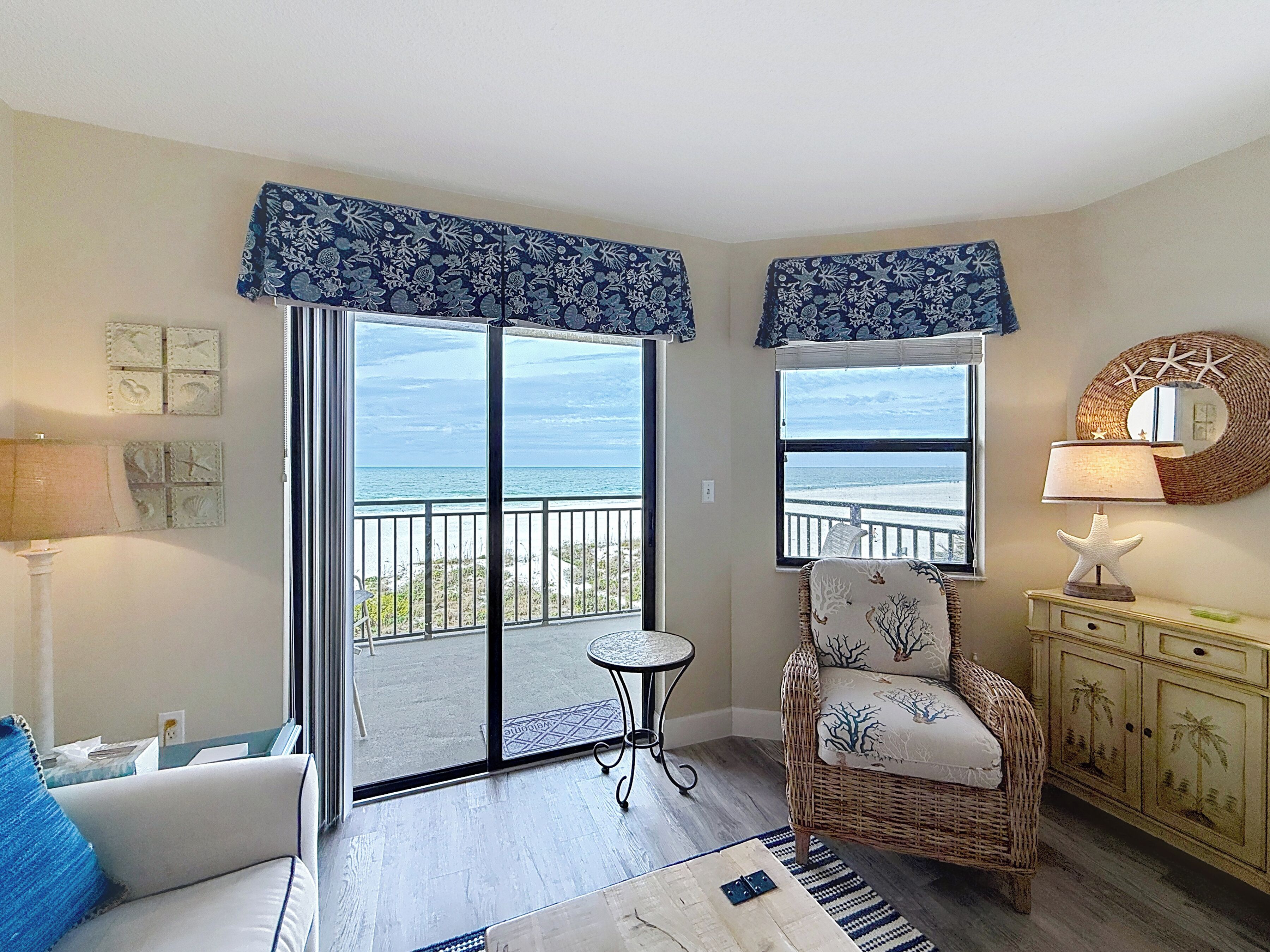 Quarto com vista para o oceano, uma cadeira de vime, uma mesa pequena e um armário com objetos decorativos.