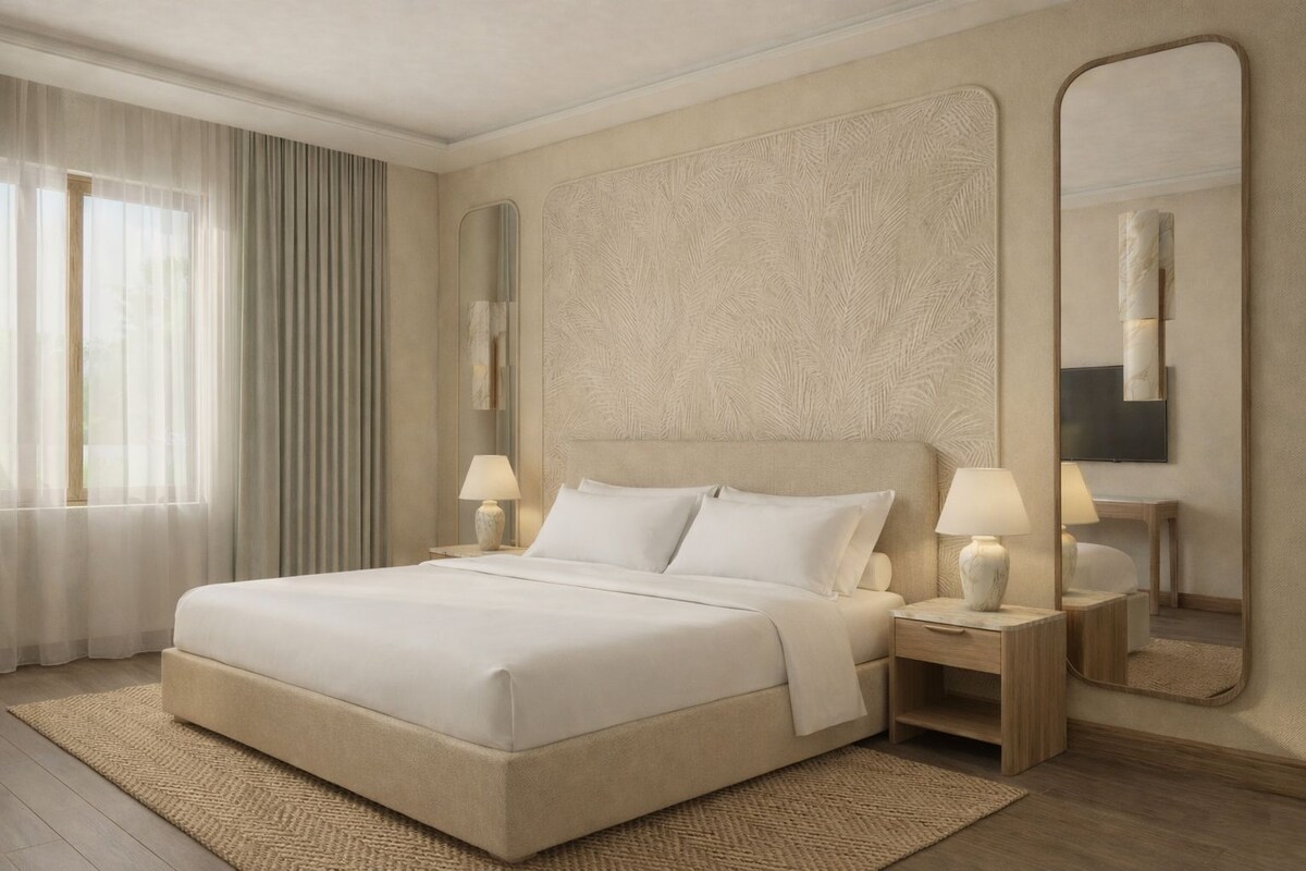 A spacious bedroom with a large bed, two bedside tables with lamps, a large mirror, and a television on the wall.