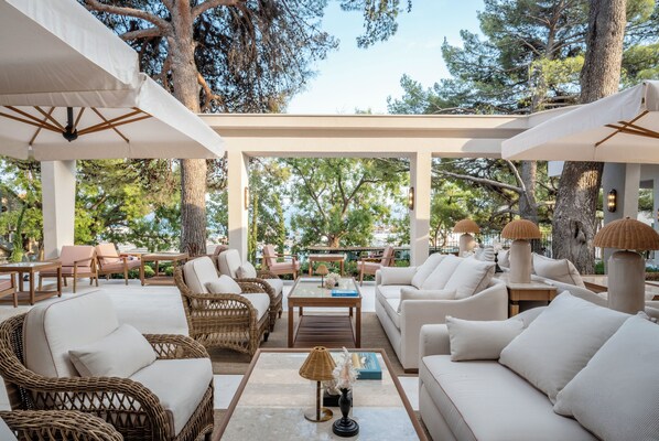An outdoor seating area with wicker furniture, white cushions, and a glass-top coffee table. - The Bristol Bol, New in 2027 (Bol)