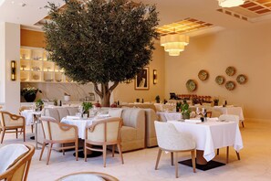 A restaurant interior with round tables, chairs, and a large tree centerpiece. - The Bristol Bol, New in 2026 (Bol)