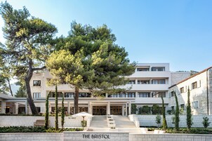 A modern hotel with a central staircase leading to the entrance, surrounded by well-maintained gardens and trees.