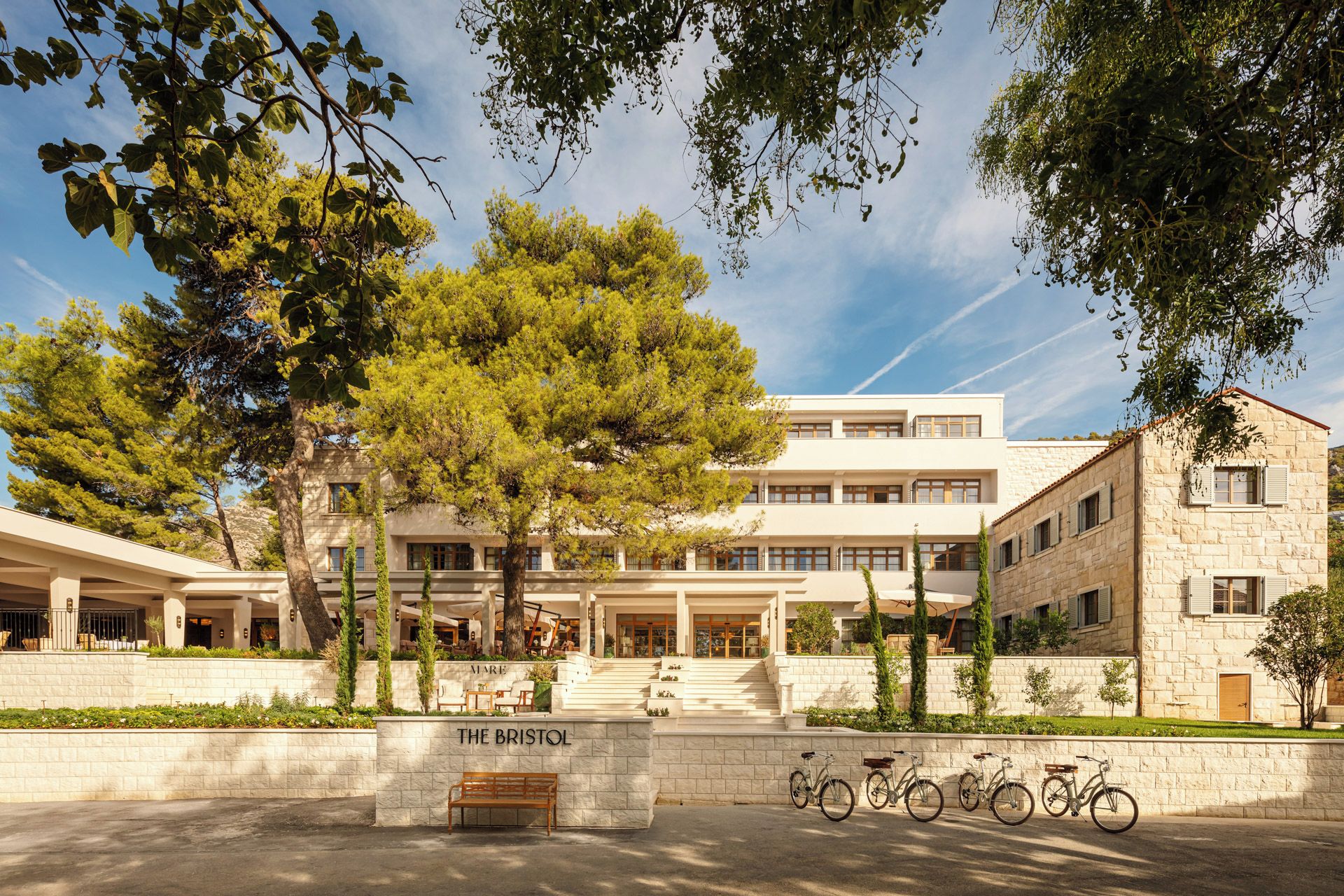 Un bâtiment moderne avec une façade en pierre, une entrée centrale avec des marches et une enseigne indiquant « THE BRISTOL ».