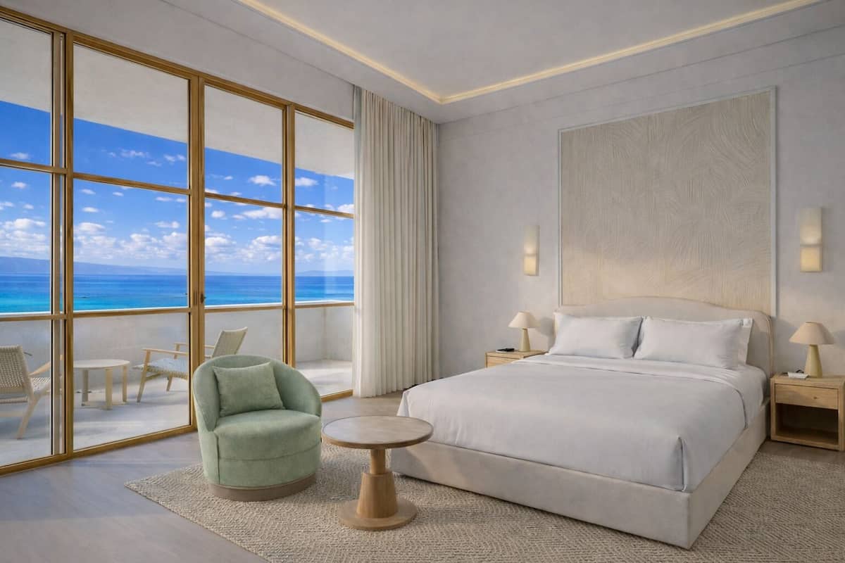 A modern hotel room with a large bed, a round table, a green armchair, and a view of the ocean.