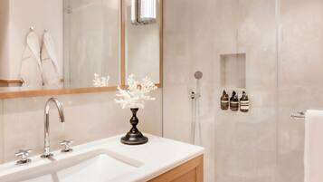 A modern bathroom with a large mirror, two sinks, a shower enclosure, and a vanity with a towel rack.