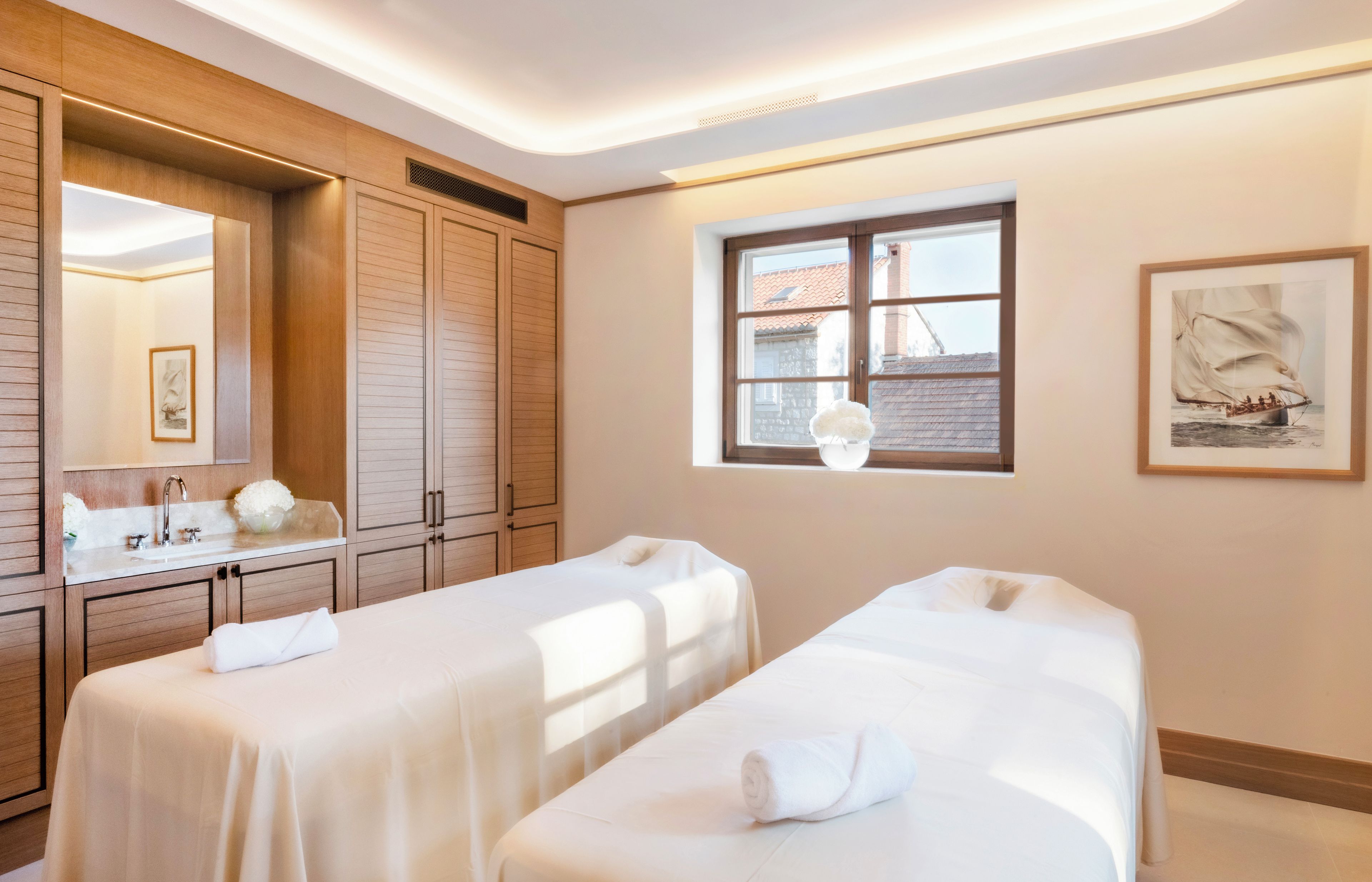 A hotel room with two beds, a large mirror, a window with a view of buildings, and a painting on the wall.