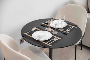 Un tavolo da pranzo rotondo con tovaglia nera, piatti bianchi, posate e un centrotavola d'argento decorativo.