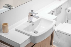 Un bagno moderno con lavandino bianco, rubinetto cromato e mobiletto in legno.