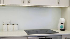 A kitchen with a built-in stove, a coffee machine, and a set of containers labeled 'SUGAR,' 'TEA,' and 'COFFEE.' - Stylish Feltham Studio near Station & Shops (Vilnius)