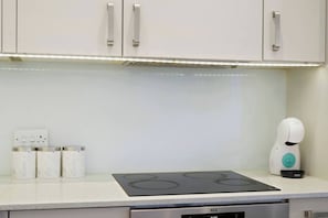 Eine Küche mit Einbauherd, Kaffeemaschine und einer Reihe Behälter, beschriftet mit 'SUGAR', 'TEA' und 'COFFEE'.