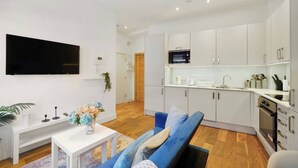 A modern living room with a sofa, a coffee table with a vase, and a flat-screen TV mounted on the wall. - Stylish Feltham Studio near Station & Shops (Vilnius)