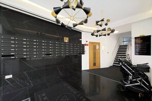 A lobby with a black marble floor, a row of black mailboxes, a wooden door, and a sign indicating the floor levels. - Stylish Feltham Studio near Station & Shops (Vilnius)