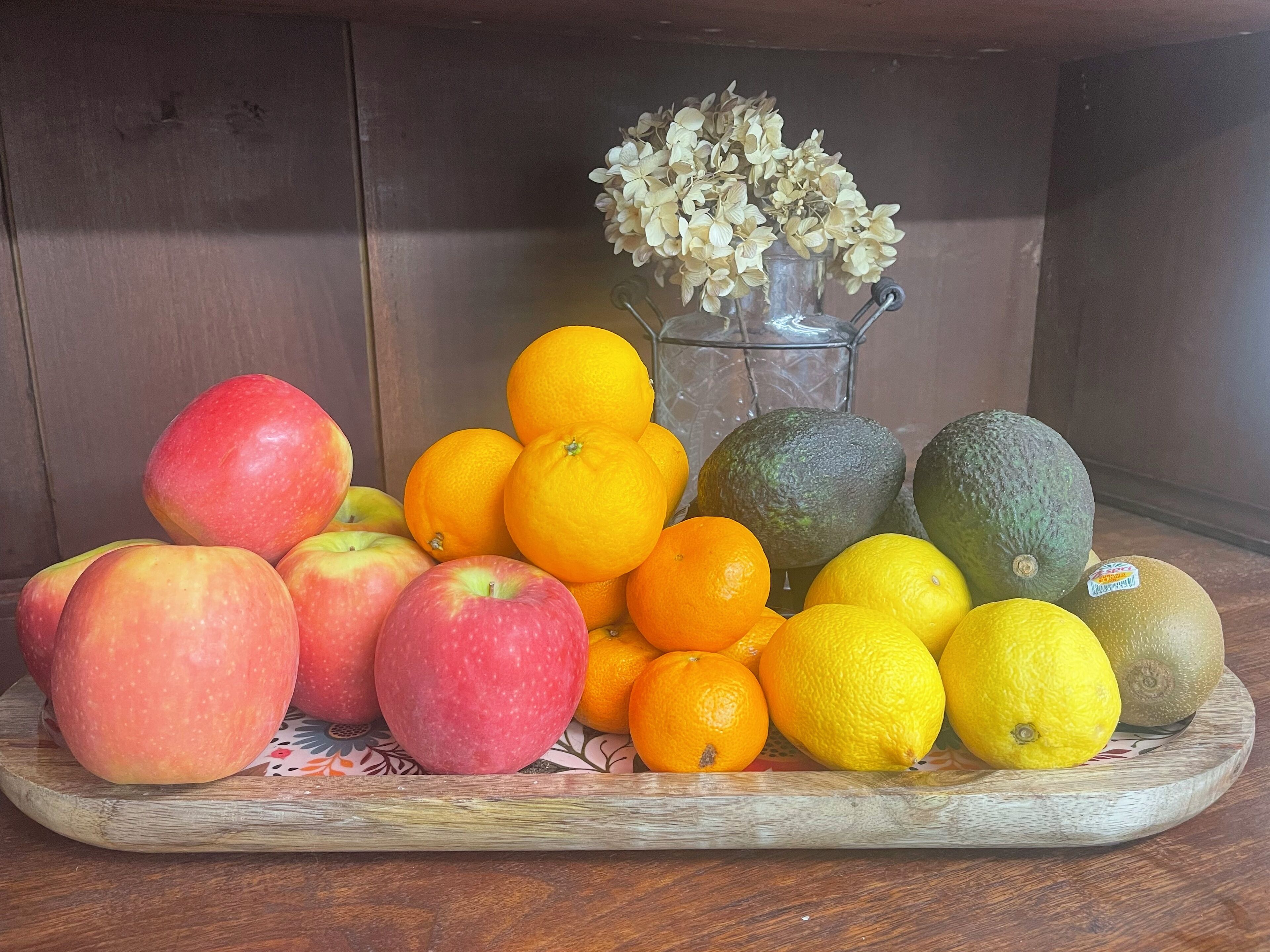 Un tavolo di legno con una varietà di frutta, tra cui mele, arance, limoni e avocado.