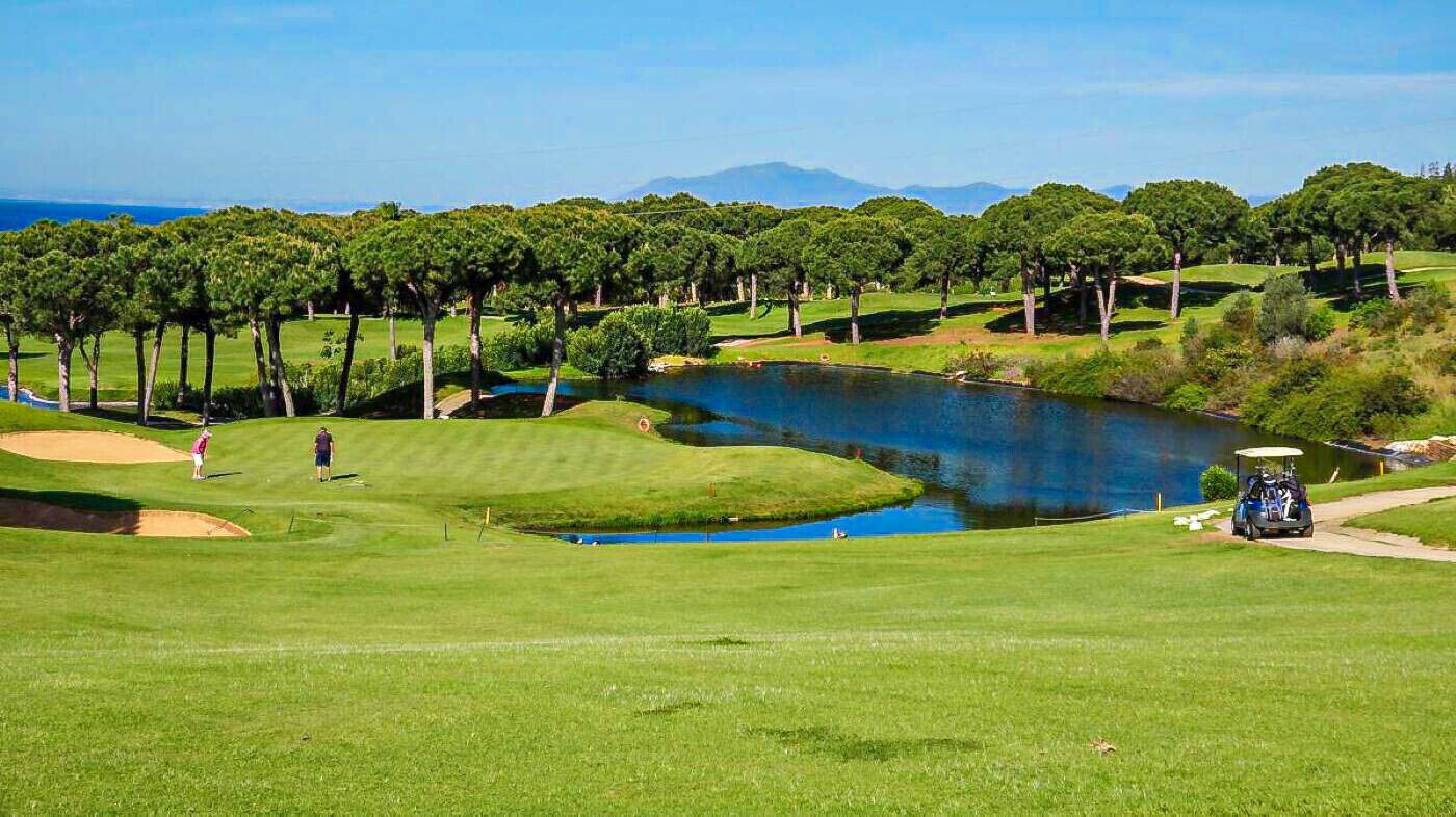 Un parcours de golf avec un étang, des arbres et un ciel dégagé.