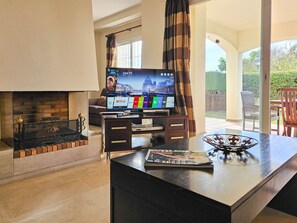 Ein modernes Wohnzimmer mit Flachbildfernseher, Kamin und Essbereich, auf dem Tisch liegt eine Zeitschrift.