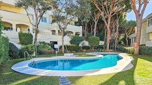 Piscina rodeada por um gramado bem cuidado e árvores, com um edifício ao fundo.