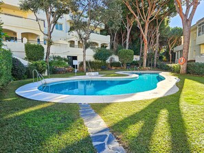 Ein Swimmingpool, umgeben von einem gepflegten Rasen und Bäumen, mit einem Gebäude im Hintergrund.