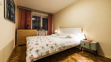 Un dormitorio con cama, cómoda, mesita de noche, ventana con cortinas y radiador.