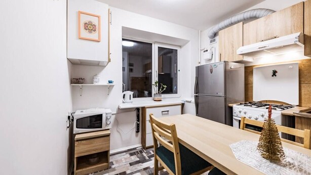 A compact kitchen with a microwave, stove, and refrigerator. There is a window above the sink and a small plant on the windowsill.