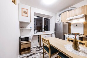 Cocina compacta con microondas, estufa y refrigerador. Hay una ventana sobre el lavamanos y una planta pequeña en el alféizar.