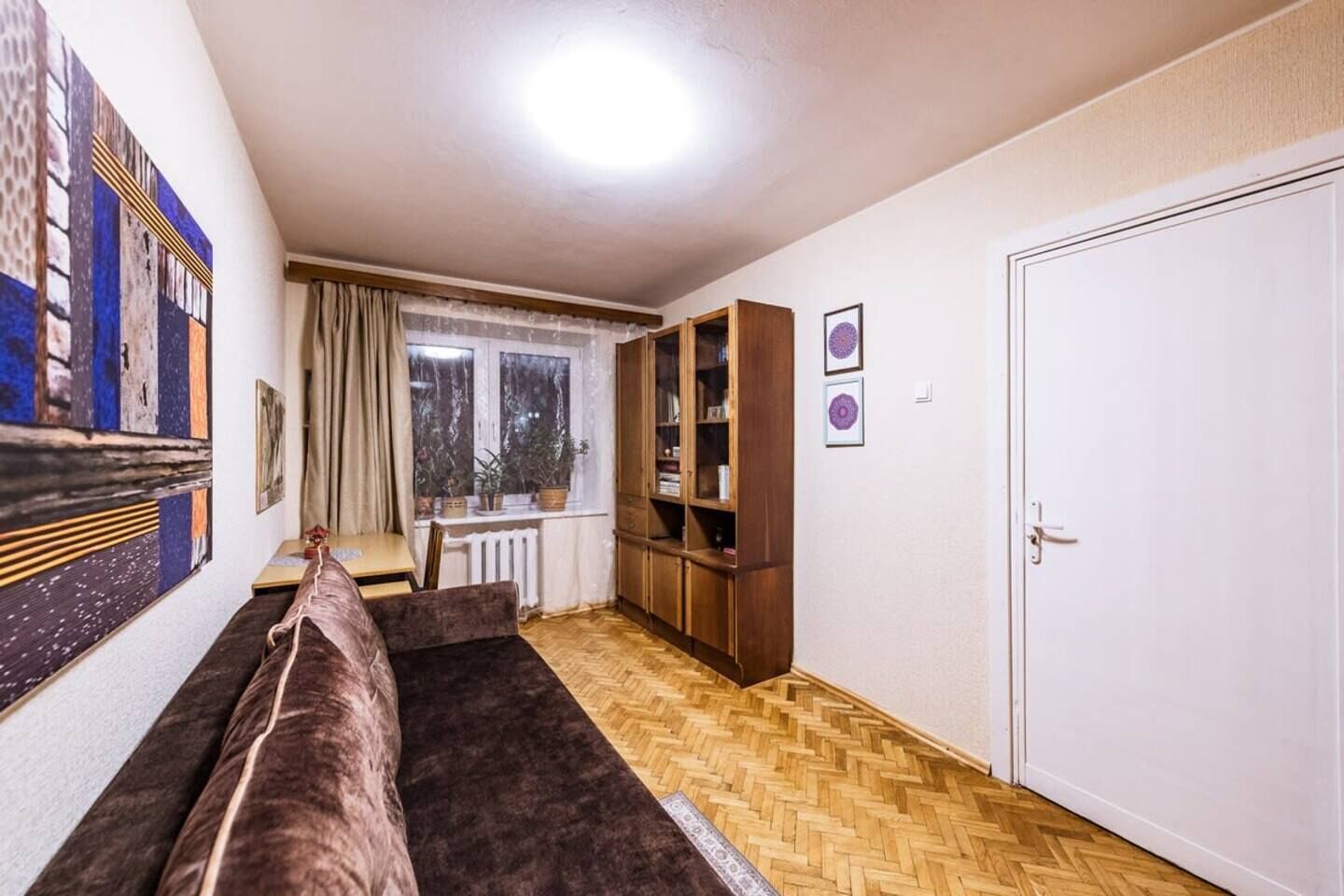 A living room with a sofa, a wooden cabinet, a window with curtains, and a door.