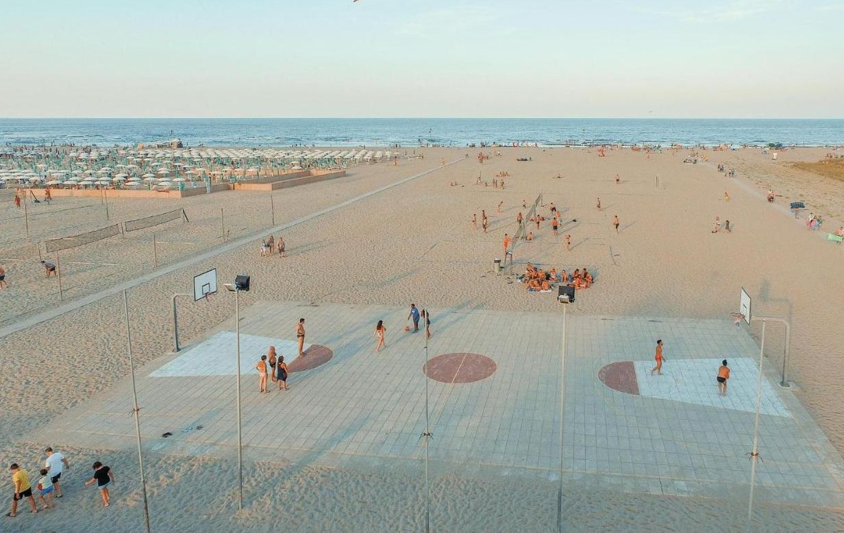 Une plage avec un terrain de volley-ball, des parasols et des gens.