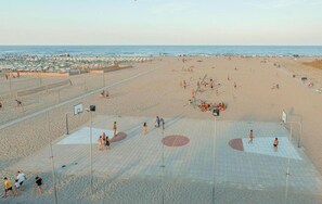 A beach with a volleyball court, umbrellas, and people. - The Charming Marina Village Tipo3-3 Bedroom Villa 6 Persons (Comacchio)
