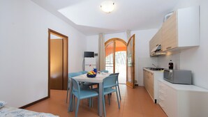 A compact room with a dining table, chairs, a bed, a kitchenette, and a door leading to a balcony. - The Charming Marina Village Tipo3-3 Bedroom Villa 6 Persons (Comacchio)