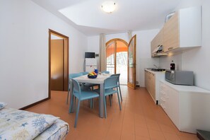 Ein gemütlicher Raum mit Esstisch, Stühlen, einem Bett, einer Küchenzeile und einer Tür, die auf einen Balkon führt.