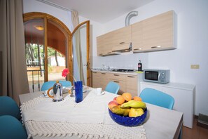 A dining area with a table set for two, a bowl of fruit, a coffee pot, and a vase with flowers. - The Charming Marina Village Tipo3-3 Bedroom Villa 6 Persons (Comacchio)
