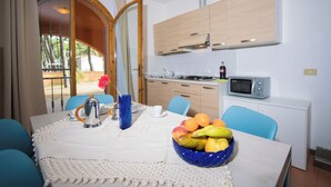 A dining area with a table set for two, a bowl of fruit, a coffee pot, and a vase with flowers. - The Charming Marina Village Tipo3-3 Bedroom Villa 6 Persons (Comacchio)