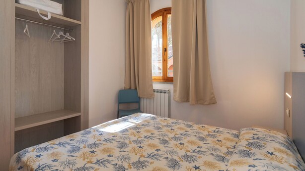 A bedroom with a bed, a wardrobe, a radiator, and a window with curtains. - The Charming Marina Village Tipo3-3 Bedroom Villa 6 Persons (Comacchio)