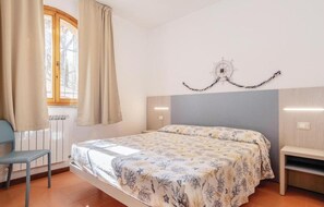 A bedroom with a bed, a chair, a window with curtains, a wall clock, and a radiator. - The Charming Marina Village Tipo3-3 Bedroom Villa 6 Persons (Comacchio)
