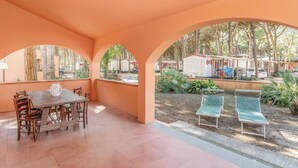 A covered outdoor area with a wooden table and chairs, two sun loungers, and a view of mobile homes in the background. - The Charming Marina Village Tipo3-3 Bedroom Villa 6 Persons (Comacchio)