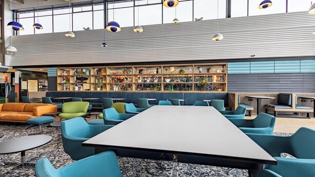 A modern lounge area with a long table, multiple seating options, and a bar area with shelves of books and decorative items. - Student Only Space St.Andrews (St. Andrews)