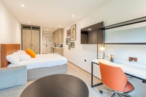 A modern hotel room with a bed, a desk, and a chair. There is a wardrobe, a mirror, and artwork on the walls. - Student Only Space St.Andrews (St. Andrews)