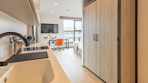 A modern kitchen with a built-in sink, a flat-screen TV mounted on the wall, and a large wooden wardrobe. - Student Only Space St.Andrews (St. Andrews)