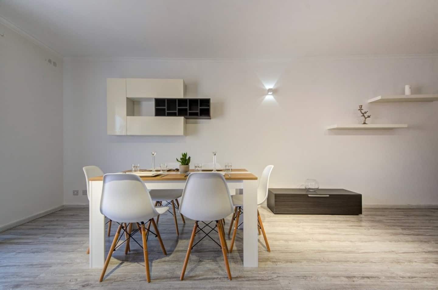 A modern dining area with a white table, four chairs, and a built-in cabinet above the table.