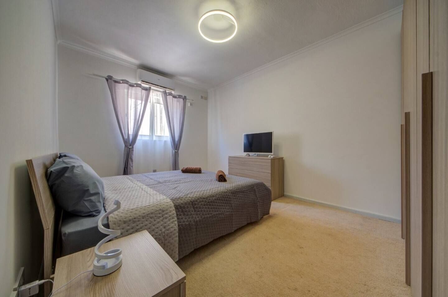A bedroom with a bed, a TV, a bedside table, and a window with curtains.