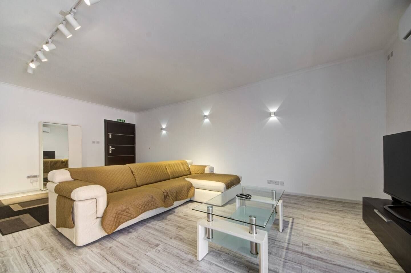 Una sala moderna con un sofá seccional, una mesa de centro de vidrio, un televisor de pantalla plana e iluminación empotrada.
