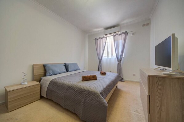 Une chambre à coucher avec un lit, des tables de chevet, une télévision et une fenêtre avec des rideaux.