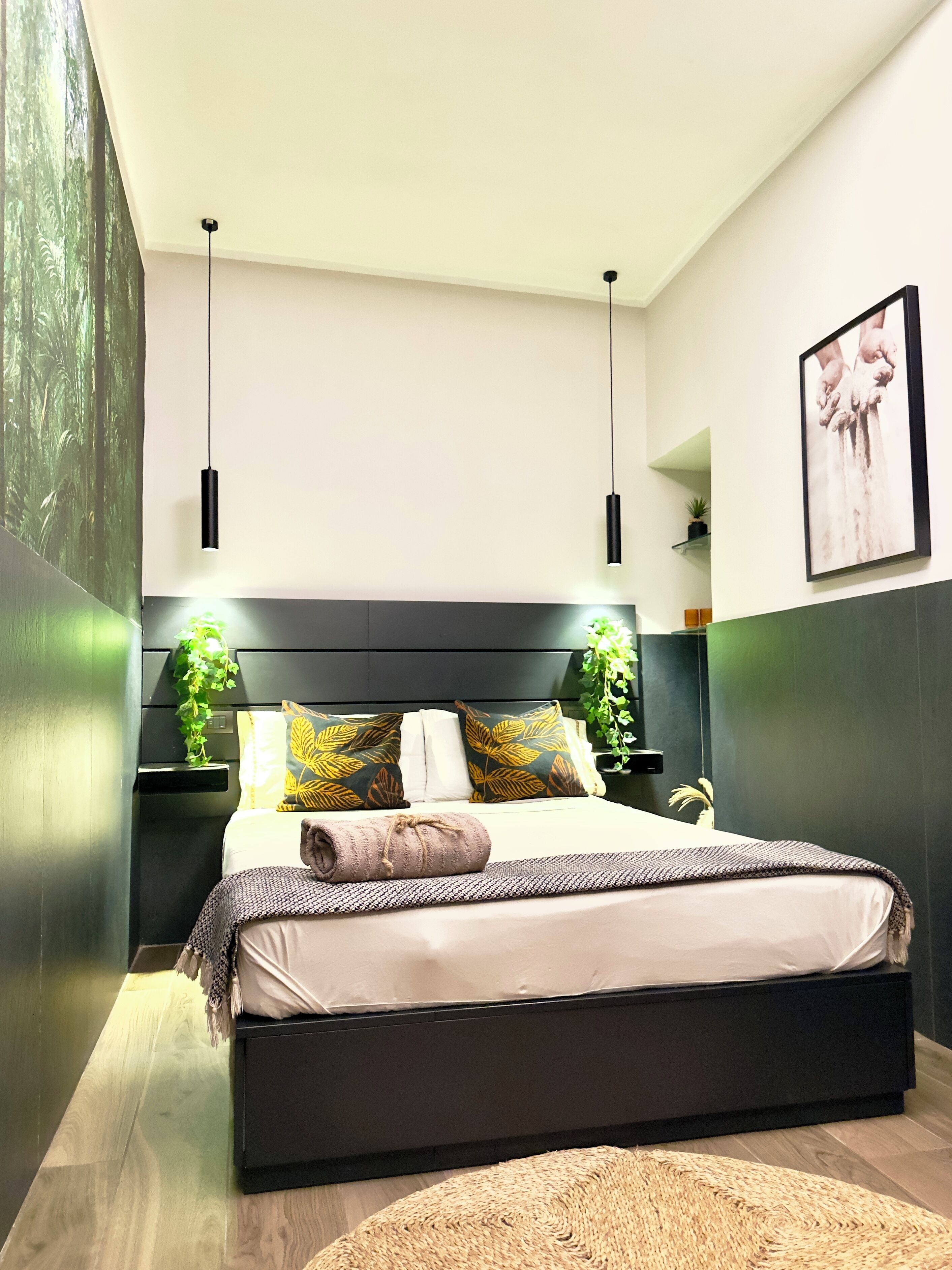A modern bedroom with a large bed, dark headboard, two pendant lights, and a framed picture on the wall.
