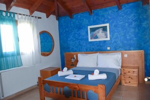 A bedroom with a wooden bed, a blue wall, a window with curtains, and a picture on the wall. - Zaros Traditional House - Private Hot Tub Retreat (Faistos)