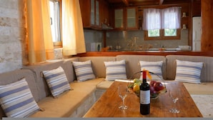 L’intérieur chaleureux d’un chalet avec une table à manger en bois, des coussins à rayures et un panier de fruits agrémenté de verres à vin.