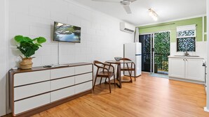 A modern kitchen with white cabinets, a wooden countertop, a ceiling fan, and a TV mounted on the wall. - Botanica Studio Edge Hill (Cairns)
