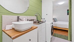 A compact hotel room with a white sink, wooden countertop, and a washing machine. - Botanica Studio Edge Hill (Cairns)