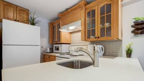 A kitchen with wooden cabinets, a stainless steel sink, a white refrigerator, a microwave, and a stove. - Comfortable Whitby 2 Bedroom Lower Suite (Whitby)