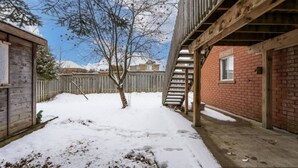 A backyard with a wooden deck, a brick building, and a wooden fence. - Comfortable Whitby 2 Bedroom Lower Suite (Whitby)